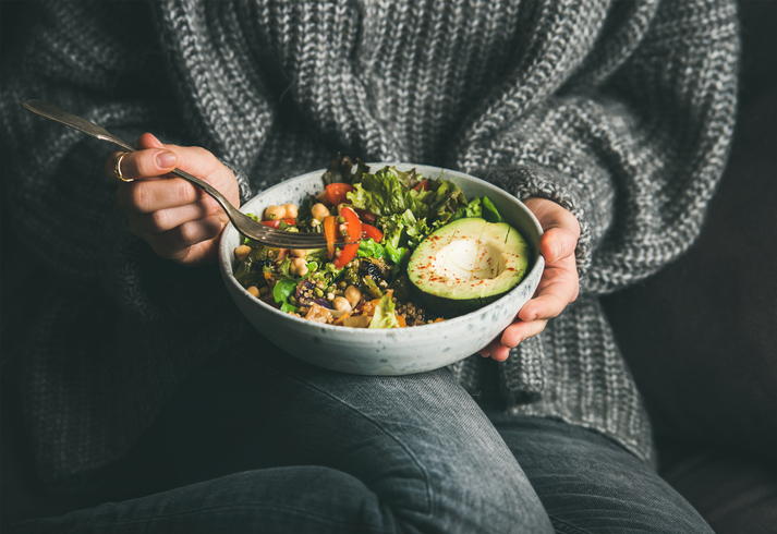 Woman in sweater eating fresh salad, avocado, beans and vegetables